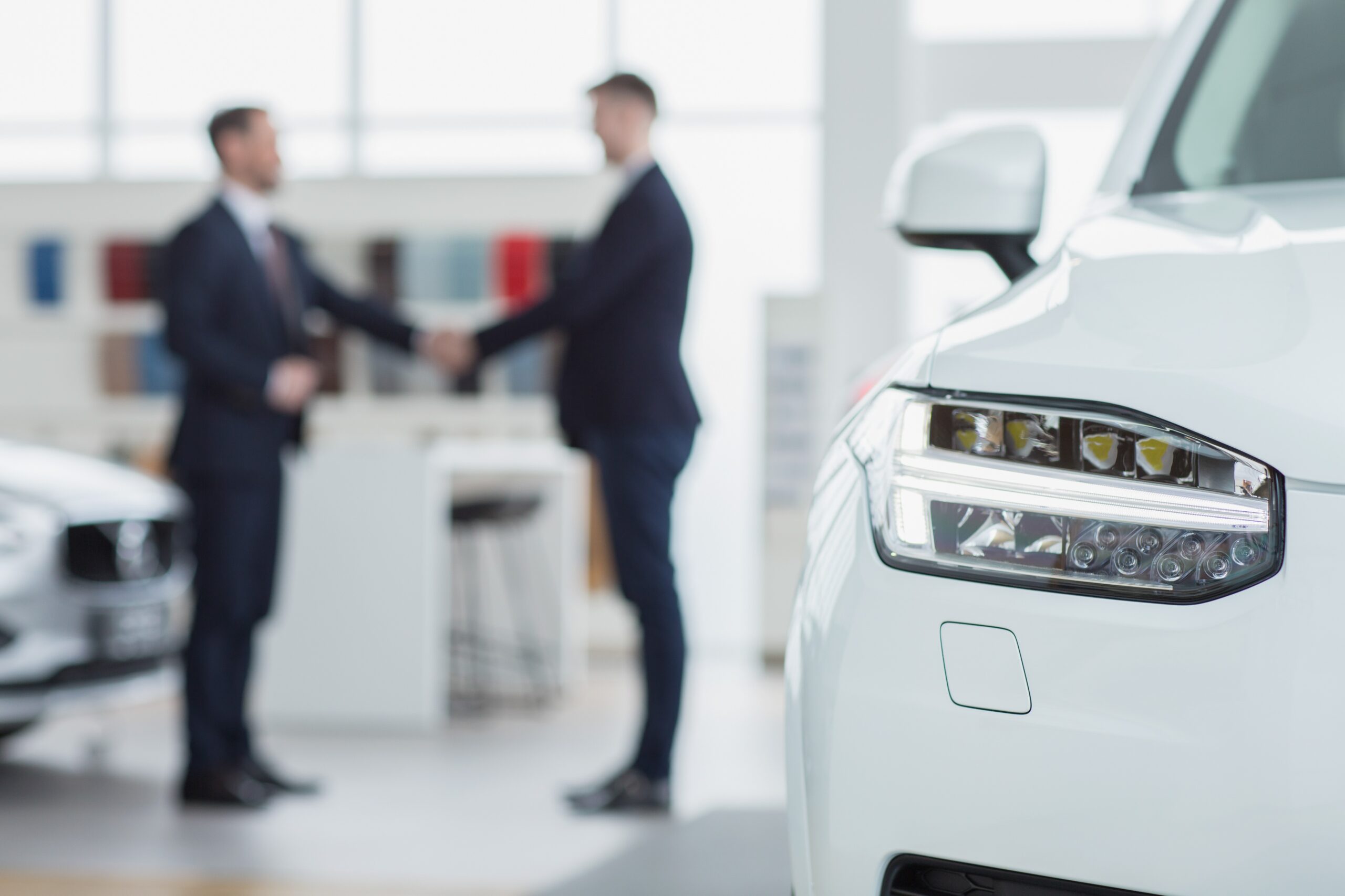 Selective focus on a car professional salesman shaking hands with his client after selling him a new automobile on the background men handshake contract deal buying agreement communicatio