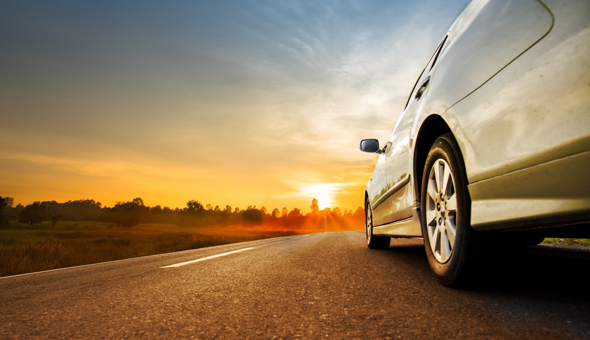 Car driving down a road towards a summer sunset