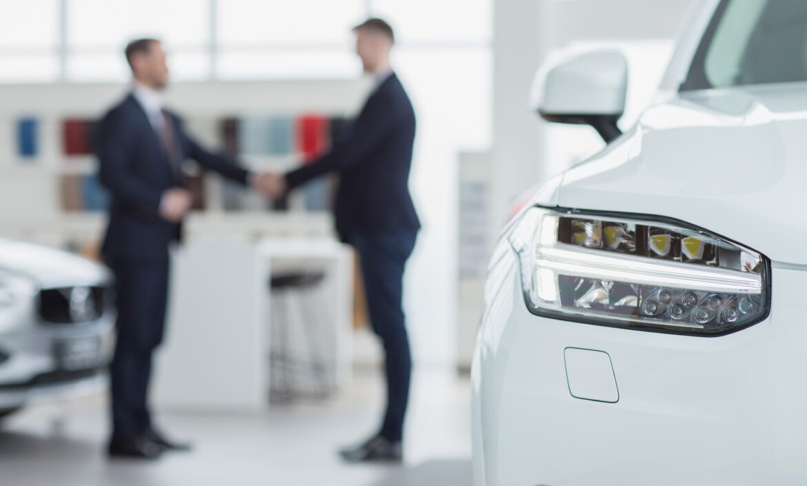 Selective focus on a car professional salesman shaking hands with his client after selling him a new automobile on the background men handshake contract deal buying agreement communicatio