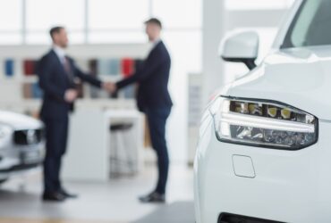 Selective focus on a car professional salesman shaking hands with his client after selling him a new automobile on the background men handshake contract deal buying agreement communicatio