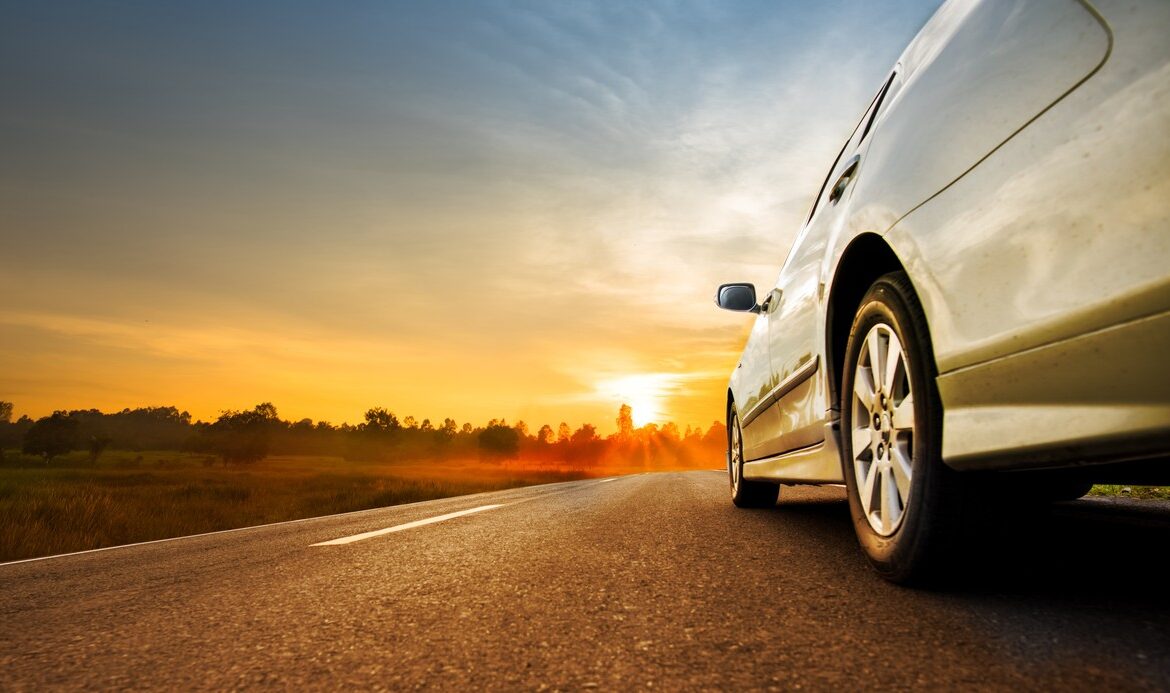 Car driving down a road towards a summer sunset