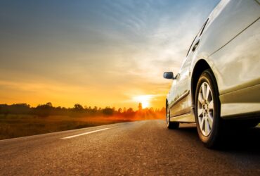 Car driving down a road towards a summer sunset